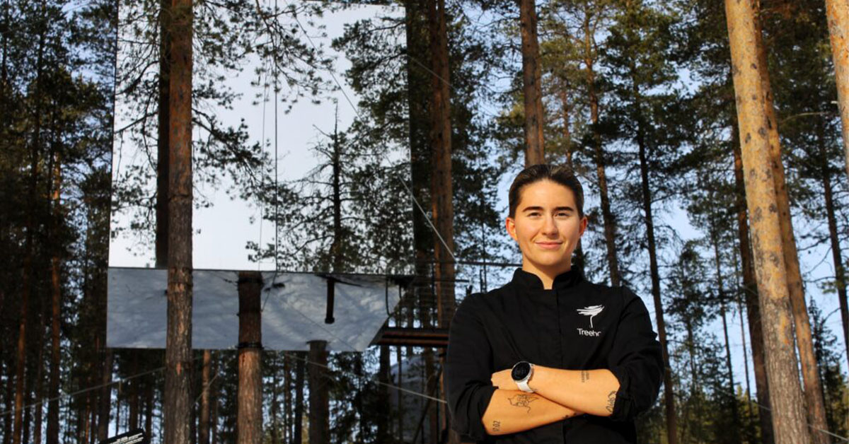 Johanna Björk iklädd svart kockrock står framför Treehotels rum Mirrorcube