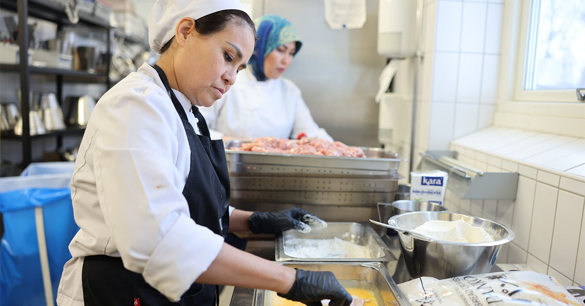 Två kvinnor i restaurangklädet förbereder mat i ett restaurangkök